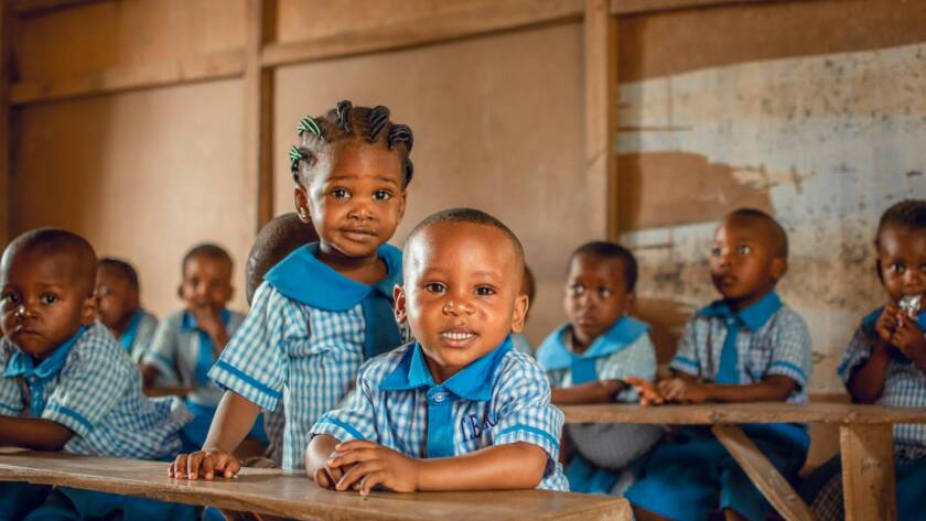 Happy children in a Nigerian classroom wearing uniforms, sitting on wooden benches.