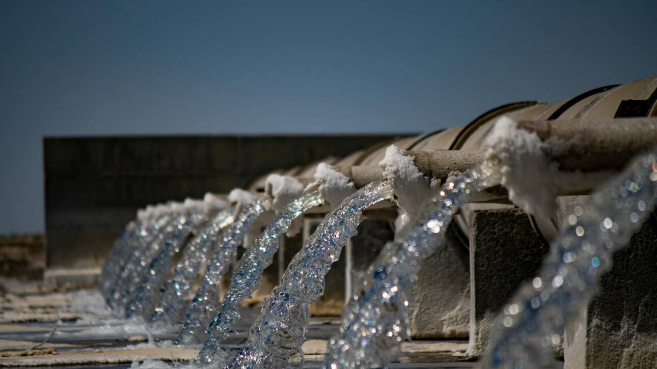 Close-up view of water flowing from industrial pipes against a clear blue sky.