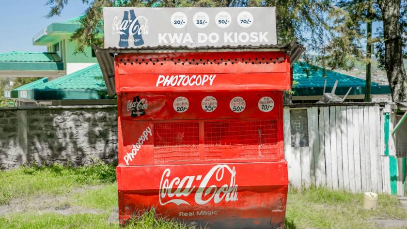 Bright Coca-Cola kiosk in a sunny Kenyan town, featuring distinct red branding.
