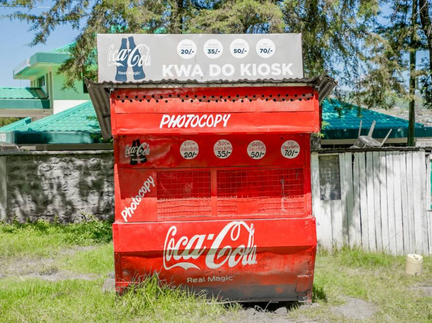 Bright Coca-Cola kiosk in a sunny Kenyan town, featuring distinct red branding.