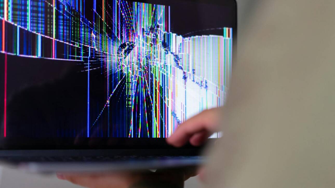 A close-up view of a cracked laptop screen displaying colorful digital distortion.