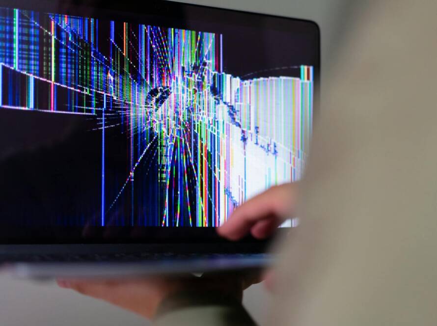 A close-up view of a cracked laptop screen displaying colorful digital distortion.