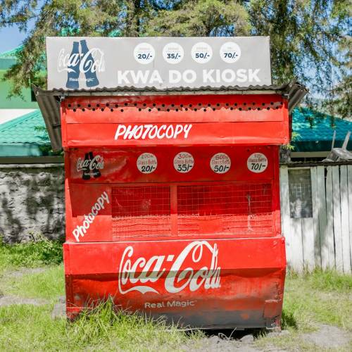Bright Coca-Cola kiosk in a sunny Kenyan town, featuring distinct red branding.